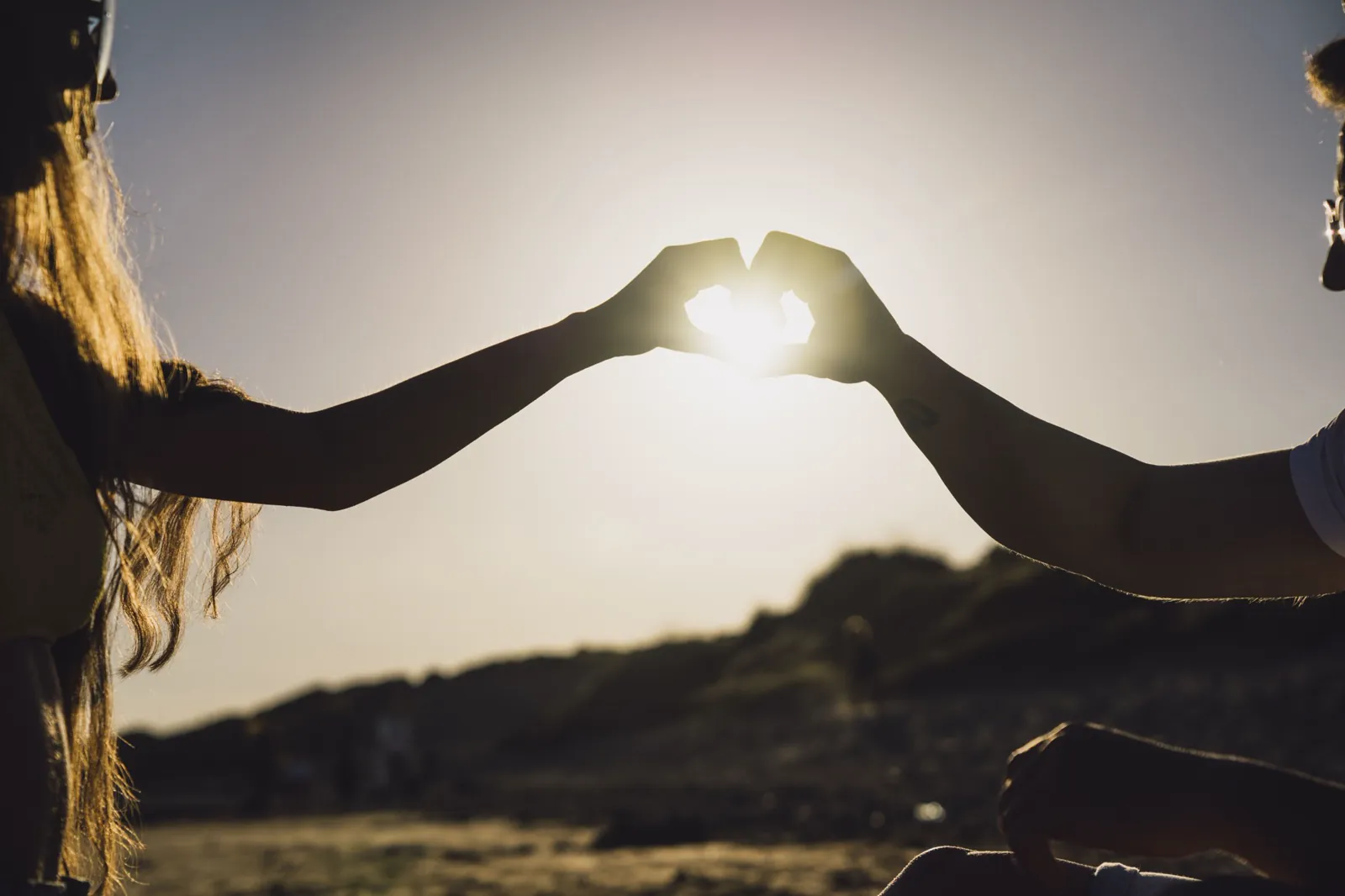 Dos manos formando un corazón a contraluz al atardecer